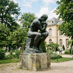 Bronze statue The Thinker seated on a stone pedestal in a garden setting